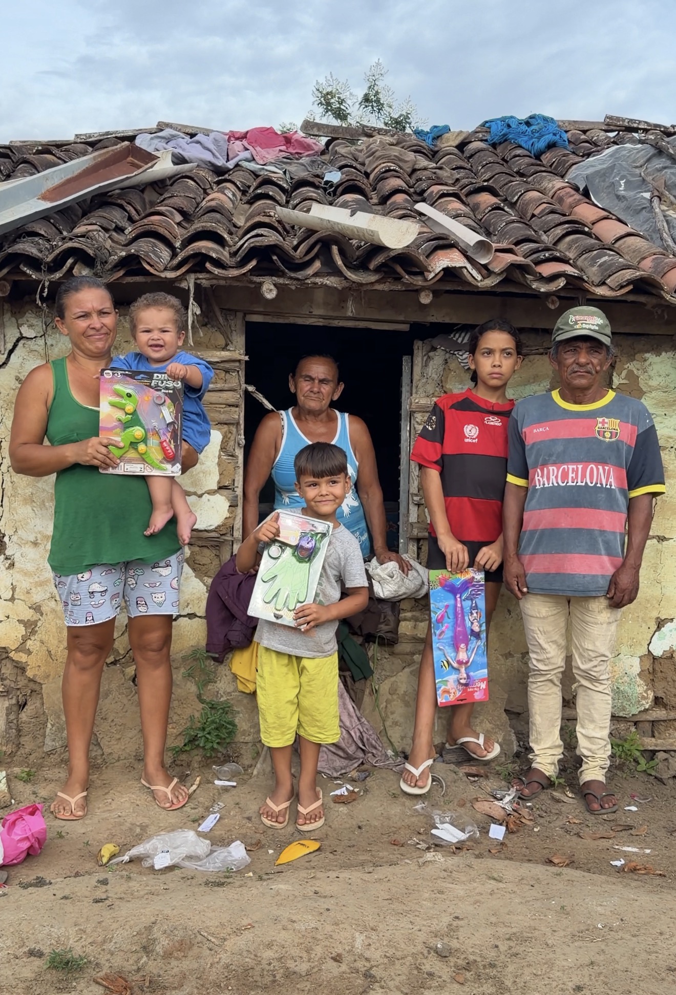 Dona Maria em frente a sua casa de taipa com sua familia segurando presentes